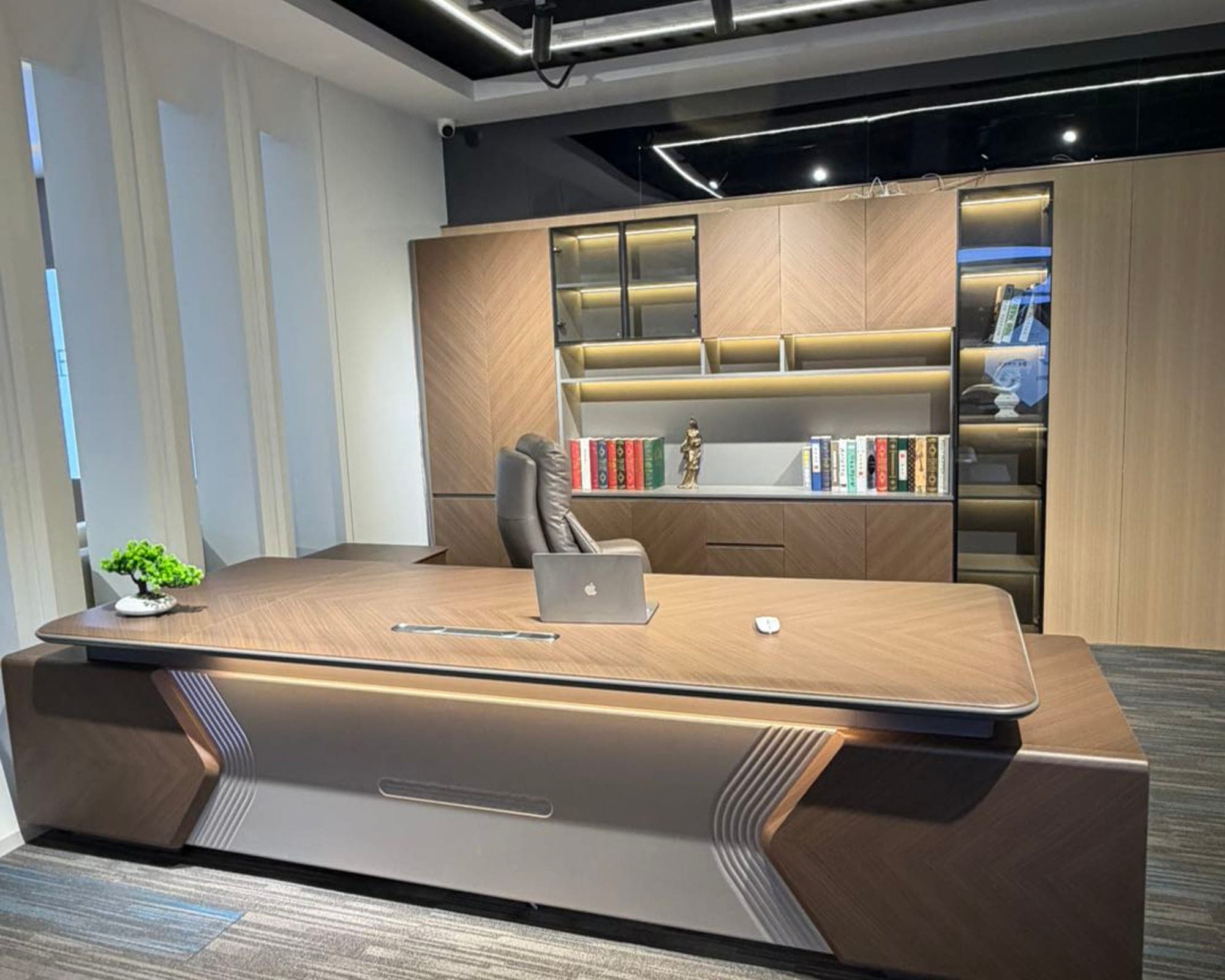 The Meridian executive desk in dark walnut under warm light, lit shelving behind