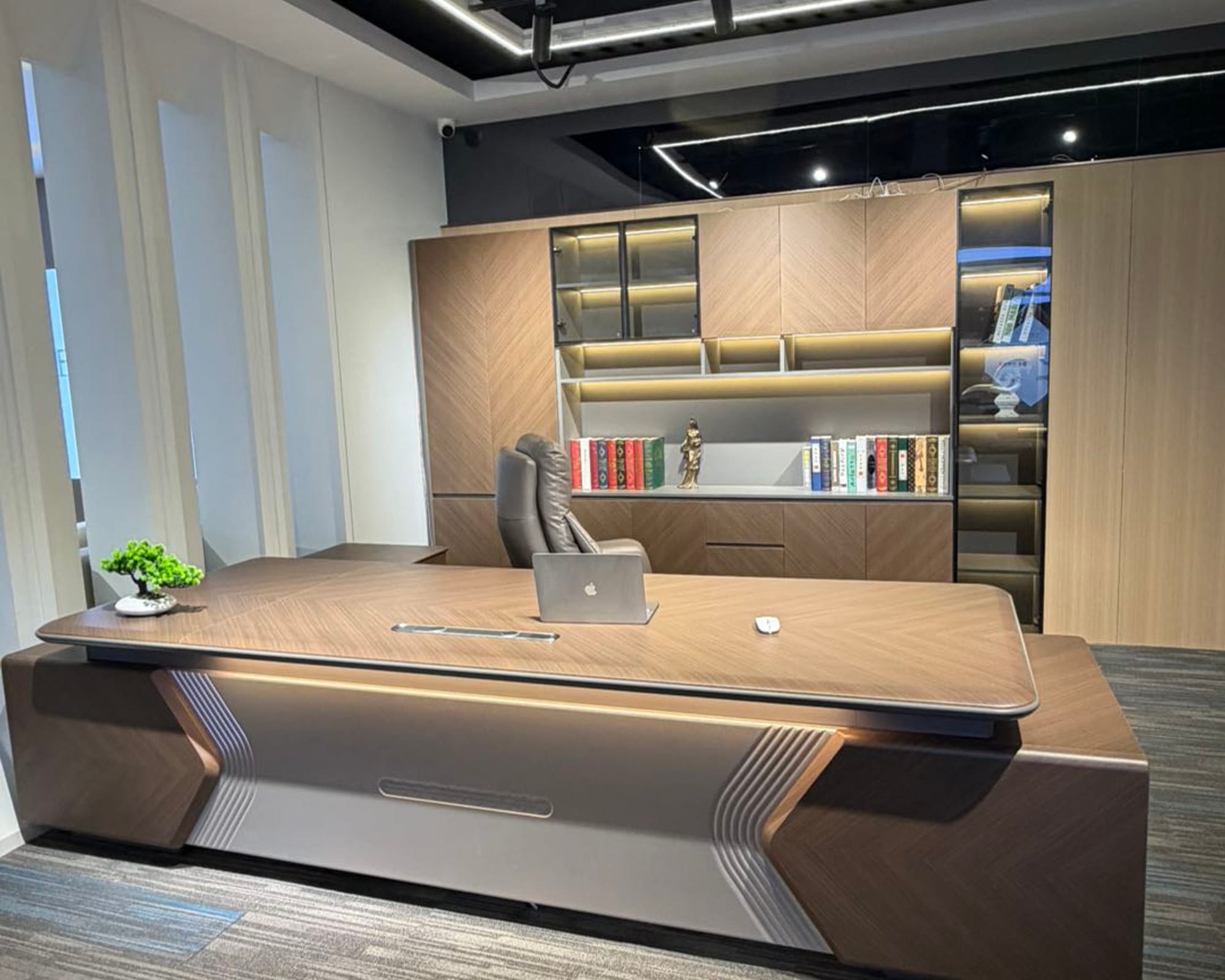 The Meridian executive desk in dark walnut under warm light, lit shelving behind
